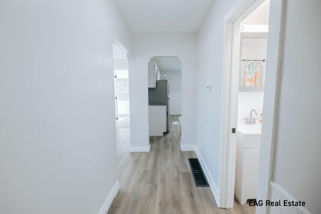 hallway featuring arched walkways, a sink, visible vents, baseboards, and light wood-type flooring