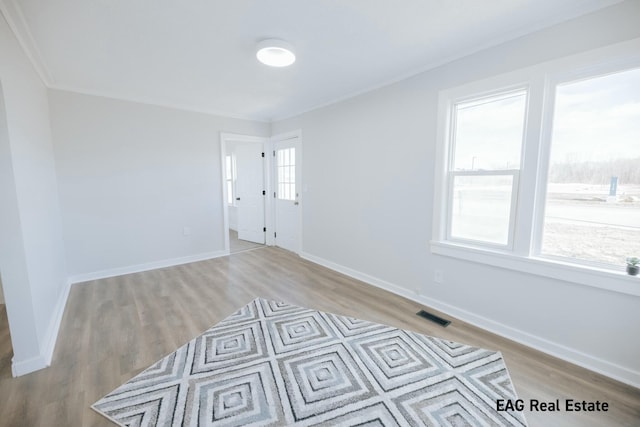 empty room featuring light wood-style floors, visible vents, crown molding, and baseboards