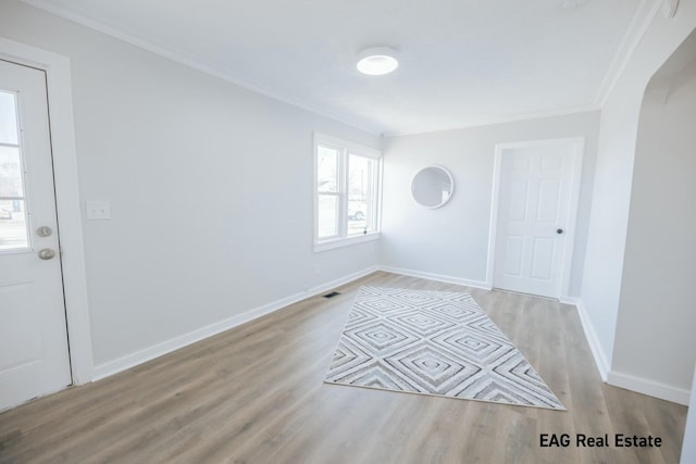 interior space with ornamental molding, arched walkways, baseboards, and wood finished floors