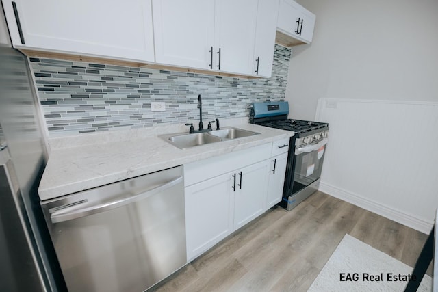 kitchen with a sink, white cabinets, appliances with stainless steel finishes, light wood-type flooring, and decorative backsplash