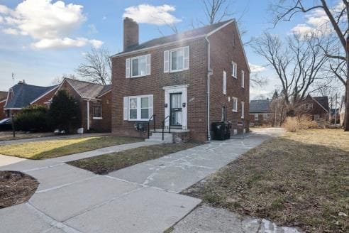 view of front of house featuring brick siding, a front lawn, and a chimney