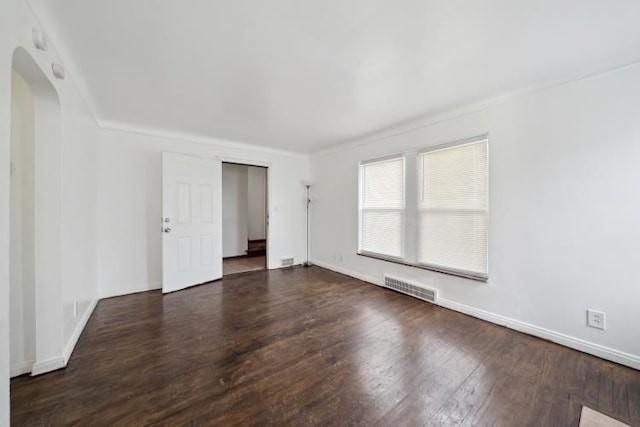 empty room with visible vents, arched walkways, baseboards, and wood finished floors