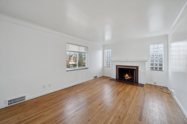 unfurnished living room featuring a brick fireplace, plenty of natural light, visible vents, and light wood-type flooring