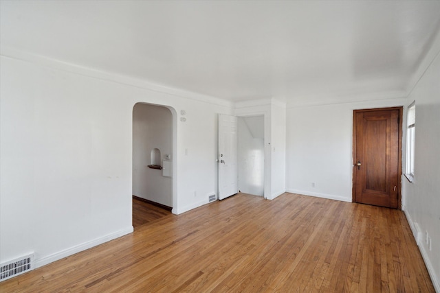 unfurnished room featuring light wood-style flooring, arched walkways, visible vents, and baseboards