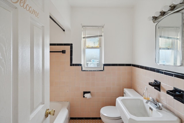 bathroom featuring toilet, a sink, a bathing tub, tile walls, and wainscoting