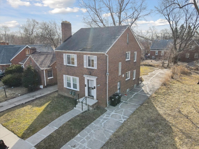 view of front of property featuring driveway, brick siding, and a chimney