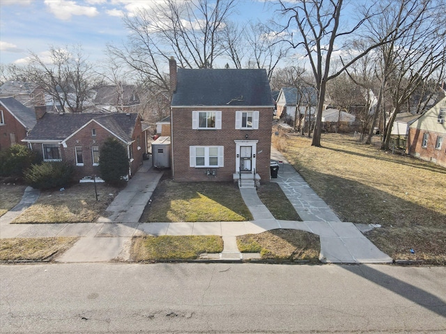 view of front facade with a front yard, a shingled roof, a chimney, concrete driveway, and brick siding