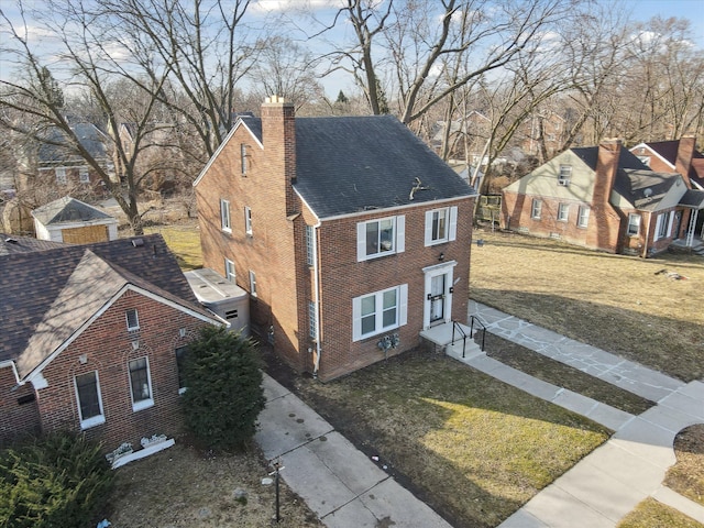 view of front of house featuring a front lawn, entry steps, roof with shingles, concrete driveway, and a chimney