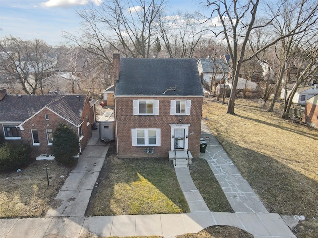 view of front facade featuring driveway, a front yard, a shingled roof, brick siding, and a chimney