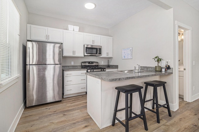 kitchen with stainless steel appliances, a peninsula, a sink, white cabinetry, and light wood-style floors