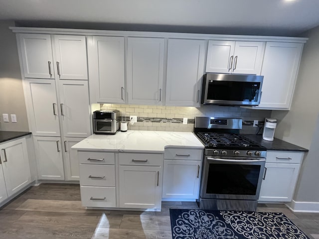 kitchen featuring appliances with stainless steel finishes, backsplash, light stone counters, and wood finished floors