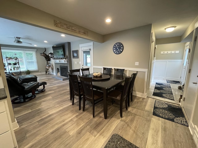 dining room with a brick fireplace, recessed lighting, wood finished floors, and wainscoting