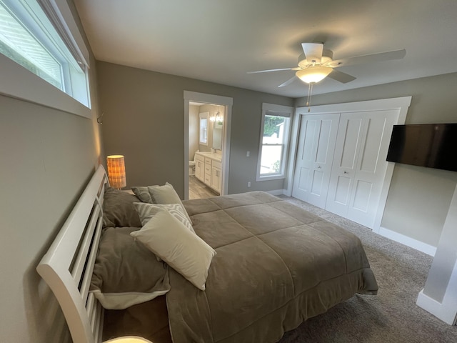 bedroom featuring light carpet, baseboards, a ceiling fan, ensuite bathroom, and a sink