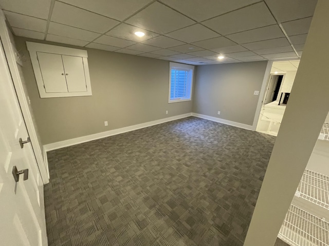 finished below grade area with dark colored carpet, a paneled ceiling, and baseboards