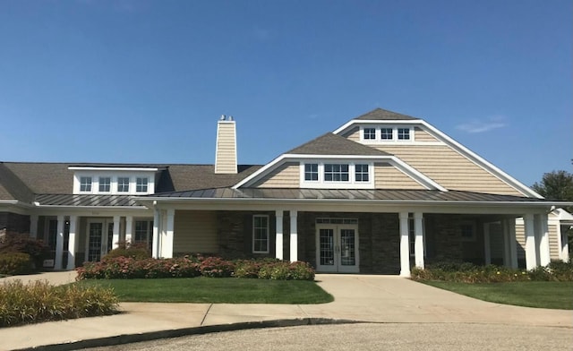 view of front of home featuring french doors, a chimney, a front yard, a standing seam roof, and metal roof