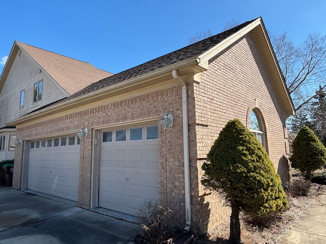 view of property exterior featuring an attached garage, brick siding, driveway, and roof with shingles