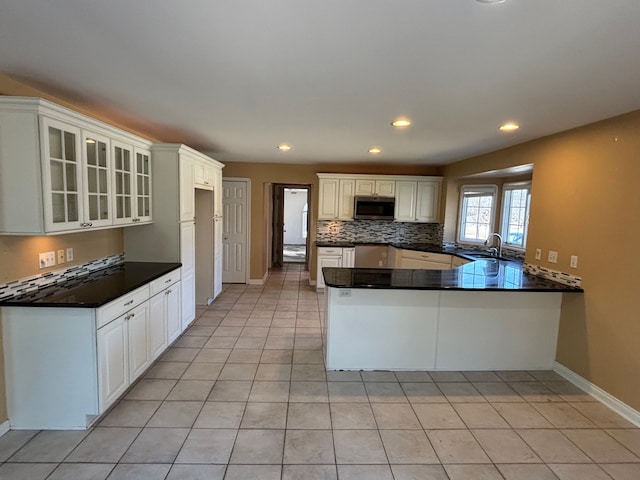 kitchen featuring a sink, stainless steel microwave, tasteful backsplash, dark countertops, and a peninsula