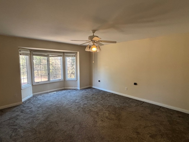 spare room with a ceiling fan, baseboards, and dark colored carpet