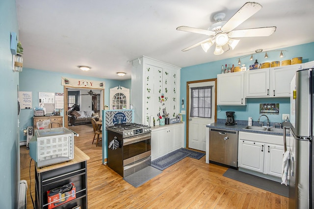 kitchen with stainless steel appliances, light wood-style flooring, a ceiling fan, white cabinets, and a sink