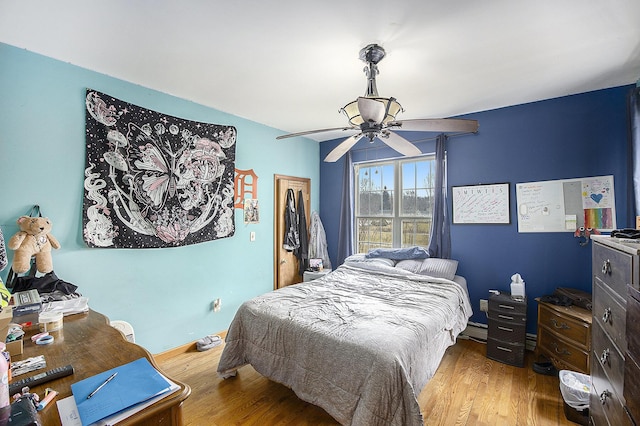 bedroom with baseboards, ceiling fan, a baseboard heating unit, and wood finished floors