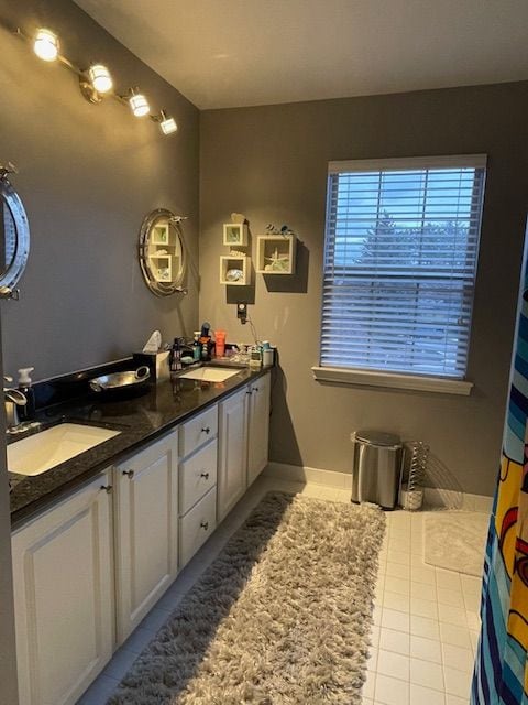 full bathroom with a sink, baseboards, double vanity, and tile patterned flooring