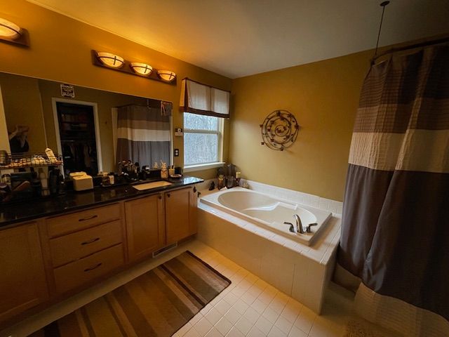 full bath with a shower with shower curtain, a garden tub, and vanity