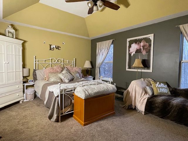 carpeted bedroom with multiple windows, a ceiling fan, and vaulted ceiling