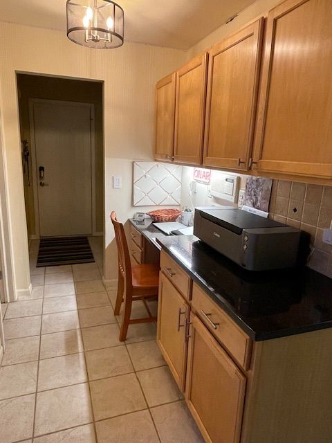 kitchen featuring dark countertops, light tile patterned floors, tasteful backsplash, and built in study area