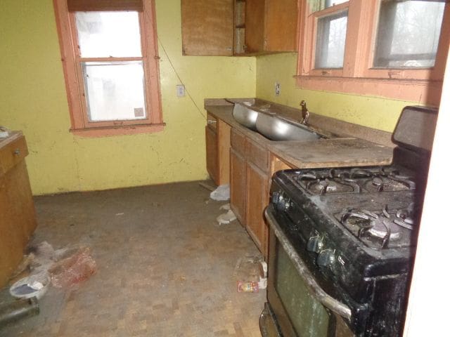 kitchen featuring gas stove, brown cabinets, and a sink