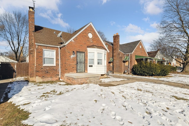 bungalow-style home featuring a chimney, fence, and brick siding