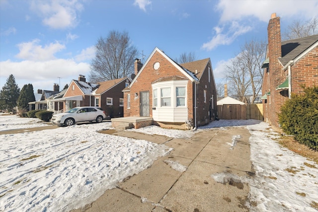 bungalow-style house featuring concrete driveway, a chimney, a residential view, fence, and brick siding