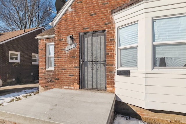 entrance to property with a shingled roof and brick siding