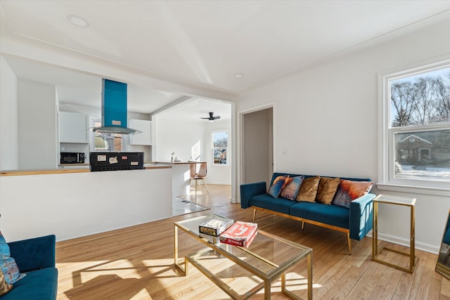 living area featuring a ceiling fan, light wood-type flooring, and baseboards