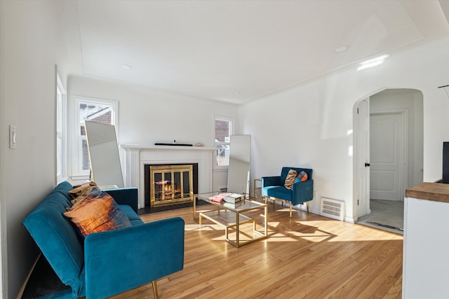 living room with arched walkways, a glass covered fireplace, wood finished floors, and visible vents