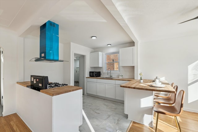 kitchen with a sink, butcher block countertops, black microwave, a peninsula, and extractor fan