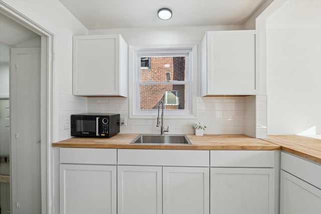 kitchen featuring butcher block countertops, black microwave, backsplash, and a sink