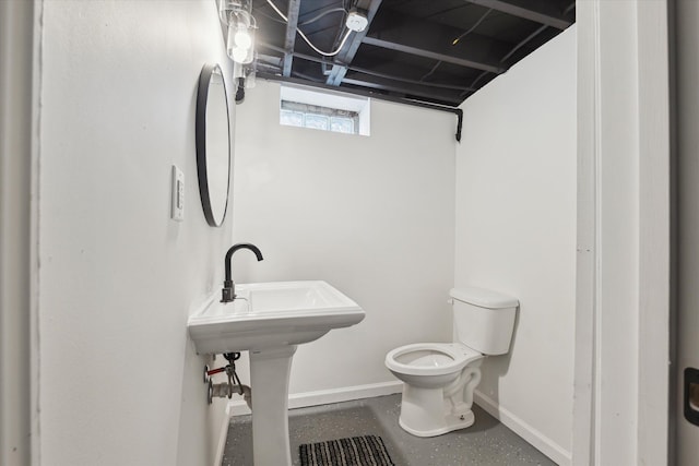 half bath featuring finished concrete floors, a sink, toilet, and baseboards