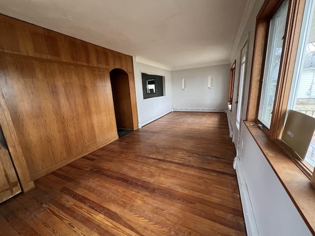 spare room with dark wood-style floors, baseboard heating, ornamental molding, and arched walkways