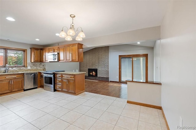 kitchen featuring open floor plan, appliances with stainless steel finishes, brown cabinetry, and light stone countertops