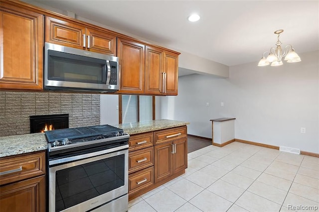 kitchen with brown cabinets, stainless steel appliances, visible vents, a brick fireplace, and light stone countertops