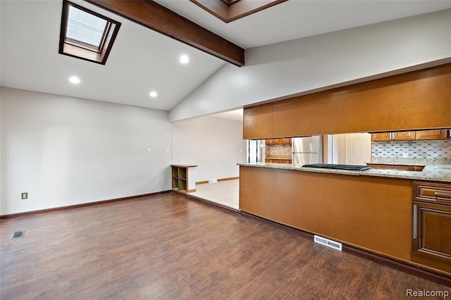 kitchen with freestanding refrigerator, brown cabinetry, backsplash, and visible vents