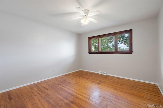 empty room with a ceiling fan, baseboards, visible vents, and wood finished floors