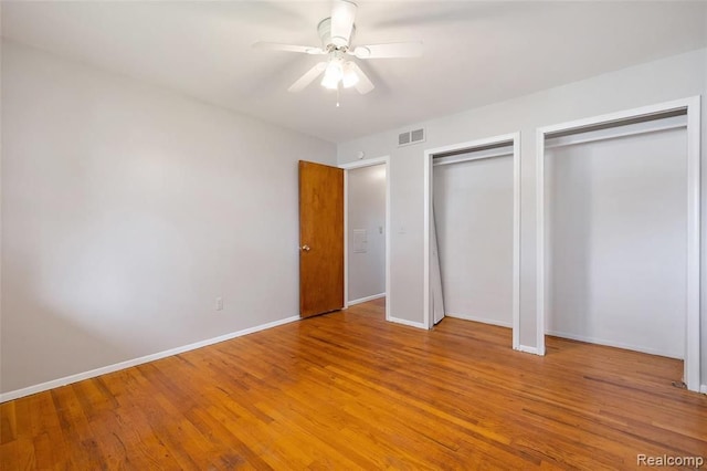 unfurnished bedroom with baseboards, wood finished floors, visible vents, and multiple closets