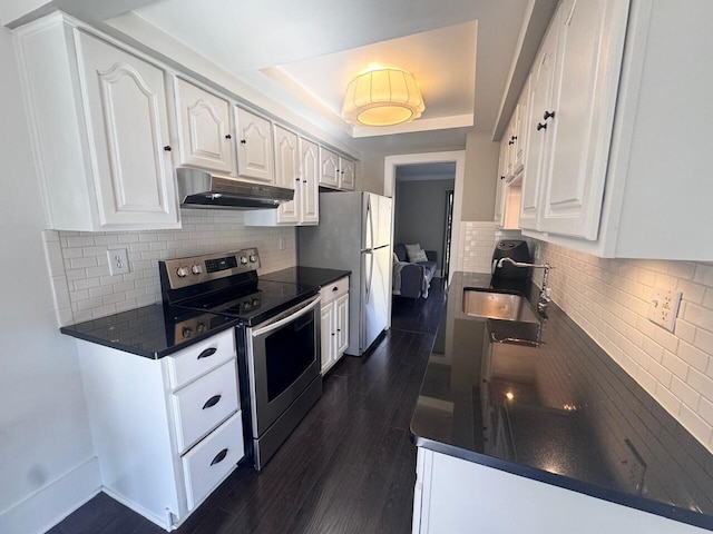 kitchen with under cabinet range hood, a sink, stainless steel electric range, a tray ceiling, and dark countertops