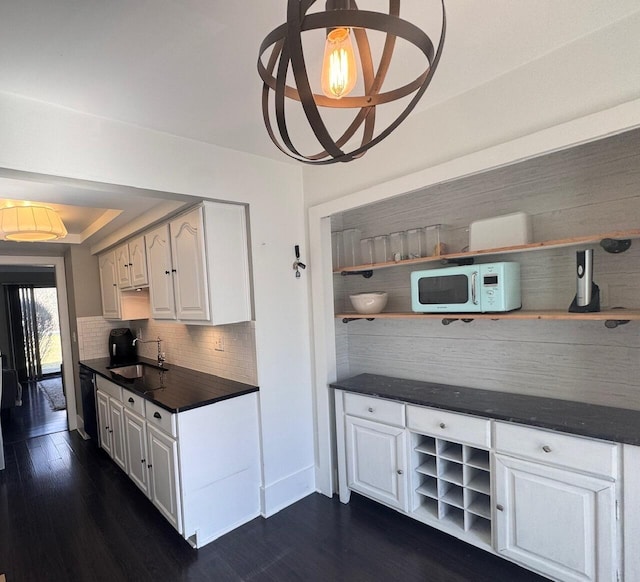 kitchen featuring dishwasher, dark countertops, white microwave, open shelves, and a sink