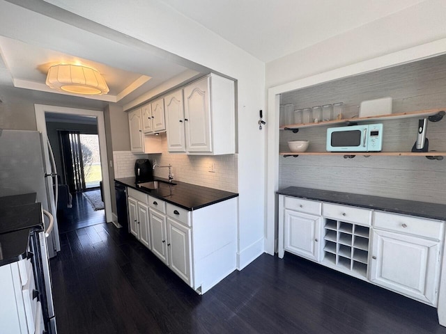 kitchen featuring white appliances, a sink, open shelves, dark countertops, and a raised ceiling