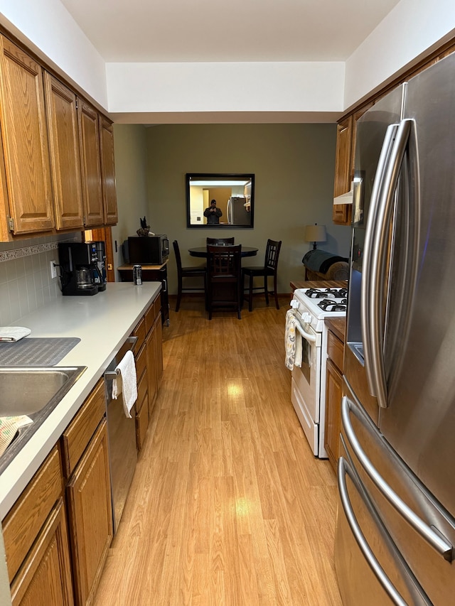 kitchen with brown cabinets, stainless steel appliances, light countertops, light wood-type flooring, and backsplash