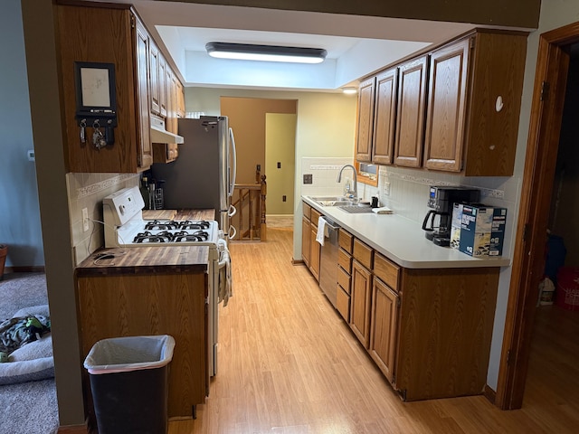 kitchen with stainless steel appliances, backsplash, light wood-style floors, a sink, and under cabinet range hood