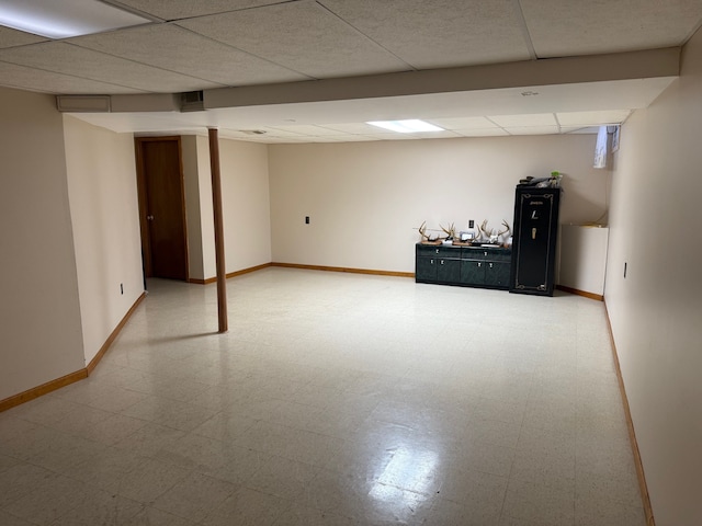 finished basement with light floors, a paneled ceiling, and baseboards