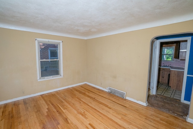 empty room with baseboards, visible vents, a textured ceiling, and hardwood / wood-style floors